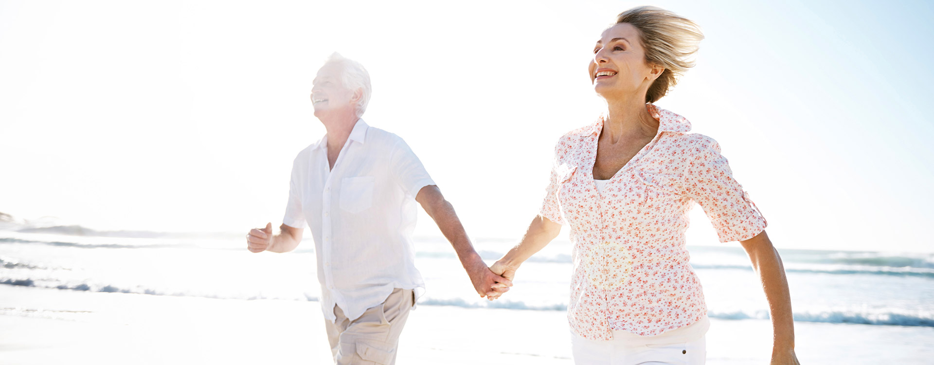 Възрастна двойка се разхожда по плажа и усмихва